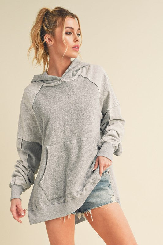 Trendy exposed seam side slit hoodie with a kangaroo pocket, perfect for a modern and relaxed casual look.