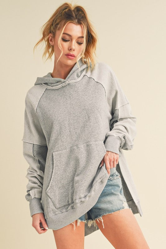 Trendy exposed seam side slit hoodie with a kangaroo pocket, perfect for a modern and relaxed casual look.