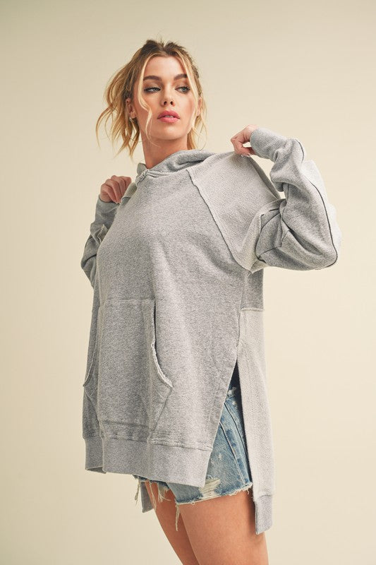 Trendy exposed seam side slit hoodie with a kangaroo pocket, perfect for a modern and relaxed casual look.