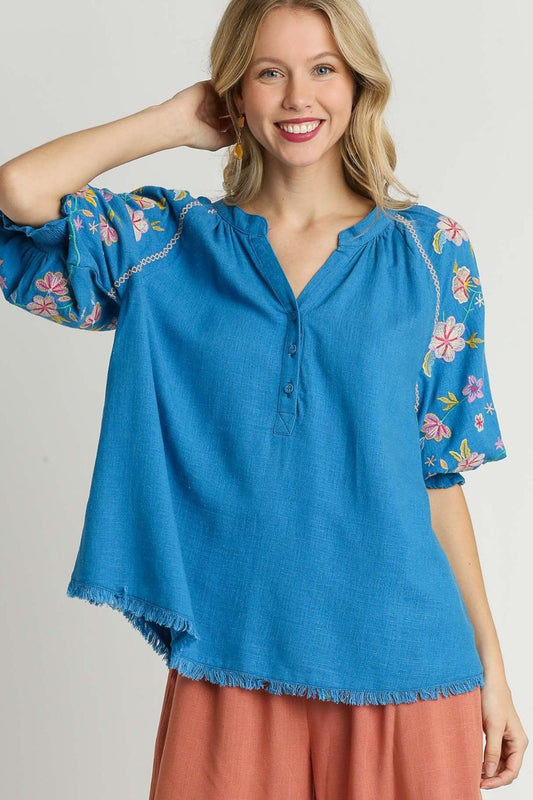 Boho-inspired half-button top with embroidered sleeves and a raw hem, perfect for a stylish and relaxed look.