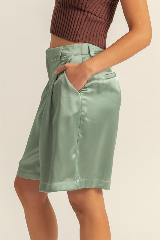 High-waist pleated satin shorts with an elegant finish, featuring a sleek design and functional pockets.